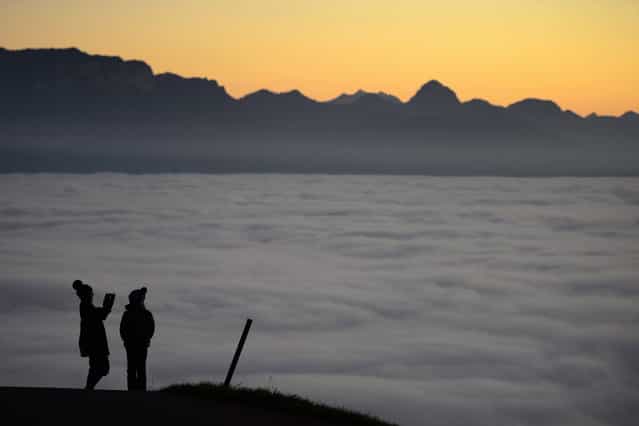 Two persons are seen in silhouette over heavy fog hanging above Lake Geneva (Lac Leman) on November 16, 2012 above Riex near Lausanne, western Switzerland. (Photo by Fabrice Coffrini/AFP Photo)