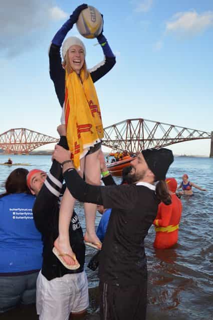 Two men lift a woman holding a rugby ball as they joined over 1,000 New Year swimmers, many in costume, braved freezing conditions in the River Forth in front of the Forth Rail Bridge during the annual Loony Dook Swim on January 1, 2013 in South Queensferry, Scotland. Thousands of people gathered last night to see in the New Year at Hogmanay celebrations in towns and cities across Scotland. (Photo by Jeff J. Mitchell)