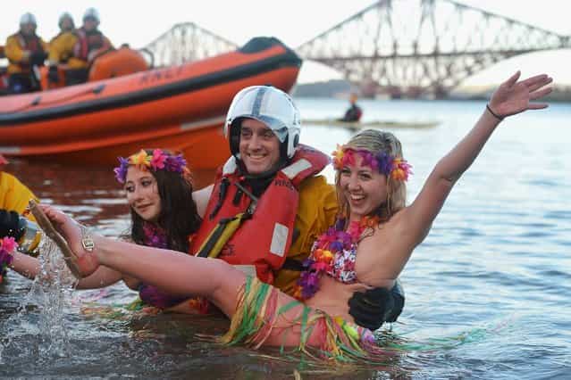 Natalie Tuccia and Sarah Johnston put their arms around a RNLI member as they joined around 1,000 New Year swimmers, many in costume, braved freezing conditions in the River Forth in front of the Forth Rail Bridge during the annual Loony Dook Swim on January 1, 2013 in South Queensferry, Scotland. Thousands of people gathered last night to see in the New Year at Hogmanay celebrations in towns and cities across Scotland.. (Photo by Jeff J. Mitchell)
