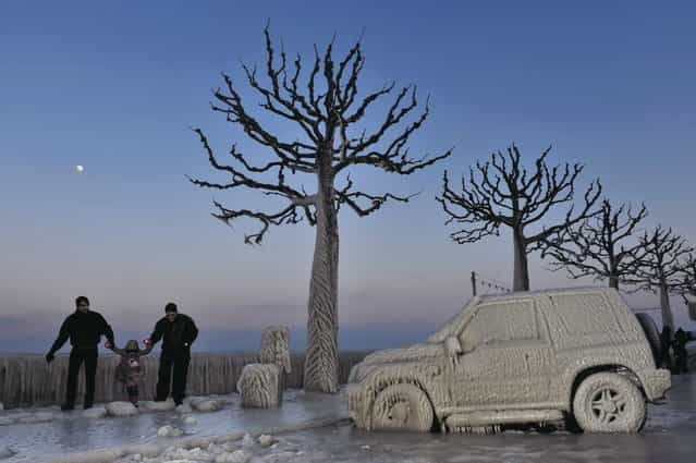 In this February 5, 2012 file photo, people walk along an icy promenade past ice covered cars and trees on the shores of Lake Geneva in Versoix, Switzerland. Across Eastern Europe, thousands of people dug out from heavy snow that had fallen during a cold snap and killed hundreds of people. (Photo by Keystone/Martial Trezzini/AP Photo)