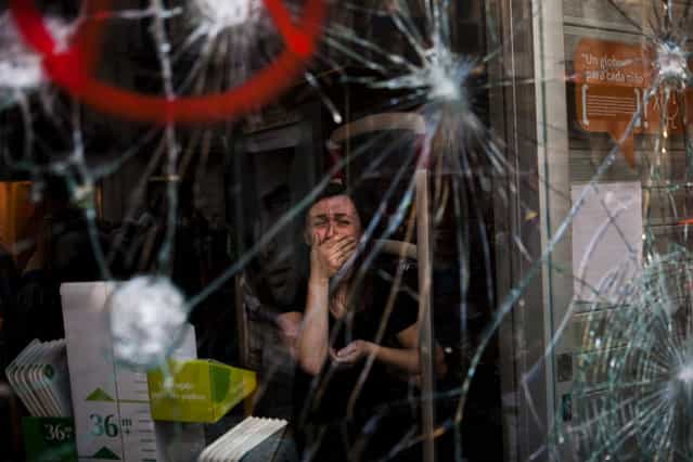 Mirian Burrueco, 30, reacts behind the broken glass of her shop stormed by demonstrators during clashes with the police at the general strike in Barcelona, Thursday, March 29, 2012. Spanish workers livid over labor reforms they see as flagrantly pro-business staged a nationwide strike Thursday and tried to bring the country to a halt by blocking traffic, closing factories and clashing with police in rowdy demonstrations. (Photo by Emilio Morenatti/AP Photo)