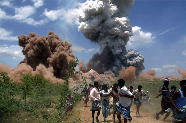 In this September 5, 2012 file photo, people run for cover as smoke rises from the site of a fire at a fireworks factory on the outskirts of Sivakasi, about 500 kilometers (310 miles) southwest of Chennai, India. Police in southern India arrested six employees of the fireworks factory for a massive blaze that killed 40 workers and injured 60 others. (Photo by AP Photo/File)