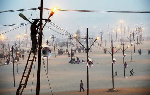 Workers fix a lightpost, one of many that will illuminate the vast grounds receiving the millions of Hindu devotees that will congregate here for the next couple of months to celebrate the Kumbh Mela, in Allahabad on January 13, 2013. Worshippers, believe a dip in the holy waters cleanses them of their sins. The Kumbh Mela in northern India, starting on January 14 and stretching over 55 days, attracts ash-covered holy men who run into the frigid waters, a smattering of international celebrities, as well as millions upon millions of ordinary Indians to Allahabad. (Photo by Roberto Schmidt/AFP Photo)