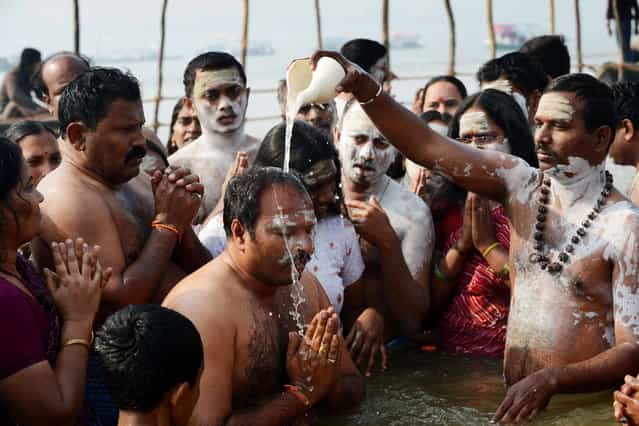A devotee has river water poured over his head at the waters edge at the Sangham or confluence of the Yamuna and Ganges river in the early morning at the Kumbh Mela celebration in Allahabad on January 13, 2013. Worshippers believe a dip in the holy waters cleanses them of their sins. The Kumbh Mela in northern India, starting January 13 and stretching over 55 days, attracts ash-covered holy men who run into the frigid waters, a smattering of international celebrities, as well as millions upon millions of ordinary Indians to Allahabad, at the confluence of the rivers Yamuna and Ganges. (Photo by Roberto Schmidt/AFP Photo)