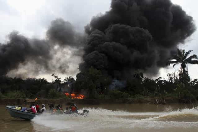 A passenger speedboat churns up the water, while in the background an illegal oil refinery is left burning after a military chase had occurred earlier in a windy creek near river Nun in Nigeria's oil state of Bayelsa December 6, 2012. Thousands of people in Nigeria engage in a practice known locally as [oil bunkering] – hacking into pipelines to steal crude then refining it or selling it abroad. The practice, which leaves oil spewing from pipelines for miles around, managed to lift around a fifth of Nigeria's two million barrel a day production last year according to the finance ministry. (Photo by Akintunde Akinleye/Reuters)