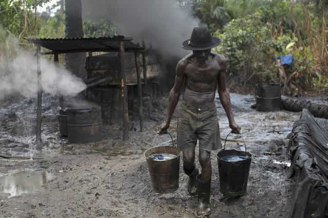 Ebiowei, 48, carries refined oil in buckets at an illegal oil refinery site near river Nun in Nigeria's oil state of Bayelsa November 27, 2012. Thousands of people in Nigeria engage in a practice known locally as 'oil bunkering' - hacking into pipelines to steal crude then refining it or selling it abroad. The practice, which leaves oil spewing from pipelines for miles around, managed to lift around a fifth of Nigeria's two million barrel a day production last year according to the finance ministry. (Photo by Akintunde Akinleye/Reuters)