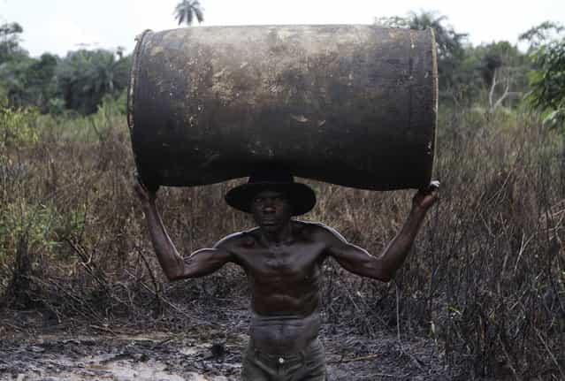 Ebiowei, 48, carries an empty oil container on his head to a place where it would be filled with refined fuel at an illegal refinery site near river Nun in Nigeria's oil state of Bayelsa November 27, 2012. Locals in the industry say workers can earn $50 to $60 a day. Thousands of people in Nigeria engage in a practice known locally as 'oil bunkering' - hacking into pipelines to steal crude then refining it or selling it abroad. The practice, which leaves oil spewing from pipelines for miles around, managed to lift around a fifth of Nigeria's two million barrel a day production last year according to the finance ministry. (Photo by Akintunde Akinleye/Reuters)