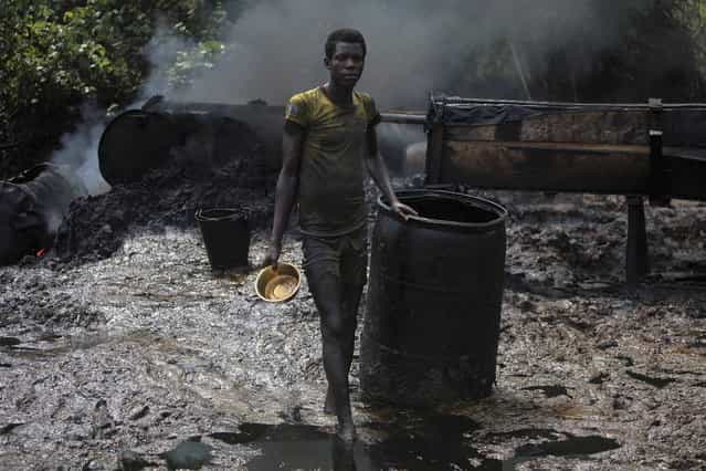 A crude oil refinery worker stands in front of a locally made burner in an illegal oil refinery site near river Nun in Nigeria's oil state of Bayelsa, November 27, 2012. The worker said that he had been doing the job for two years and earned the equivalent of around $60 a day. Thousands of people in Nigeria engage in a practice known locally as 'oil bunkering' - hacking into pipelines to steal crude then refining it or selling it abroad. The practice, which leaves oil spewing from pipelines for miles around, managed to lift around a fifth of Nigeria's two million barrel a day production last year according to the finance ministry. (Photo by Akintunde Akinleye/Reuters)