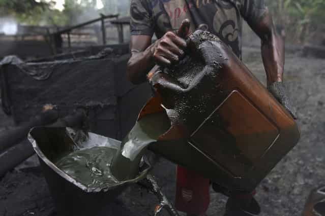 A worker pours crude oil into a locally made burner using a funnel at an illegal oil refinery site near river Nun in Nigeria's oil state of Bayelsa November 25, 2012. Thousands of people in Nigeria engage in a practice known locally as [oil bunkering] – hacking into pipelines to steal crude then refining it or selling it abroad. The practice, which leaves oil spewing from pipelines for miles around, managed to lift around a fifth of Nigeria's two million barrel a day production last year according to the finance ministry. (Photo by Akintunde Akinleye/Reuters)