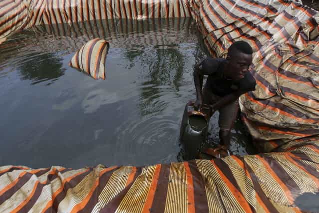 A man named Godswill collects crude oil from a mini storage unit filled with oil, which is waiting to be refined at an illegal refinery site near river Nun in Nigeria's oil state of Bayelsa November 27, 2012. Thousands of people in Nigeria engage in a practice known locally as 'oil bunkering' - hacking into pipelines to steal crude then refining it or selling it abroad. The practice, which leaves oil spewing from pipelines for miles around, managed to lift around a fifth of Nigeria's two million barrel a day production last year according to the finance ministry. (Photo by Akintunde Akinleye/Reuters)