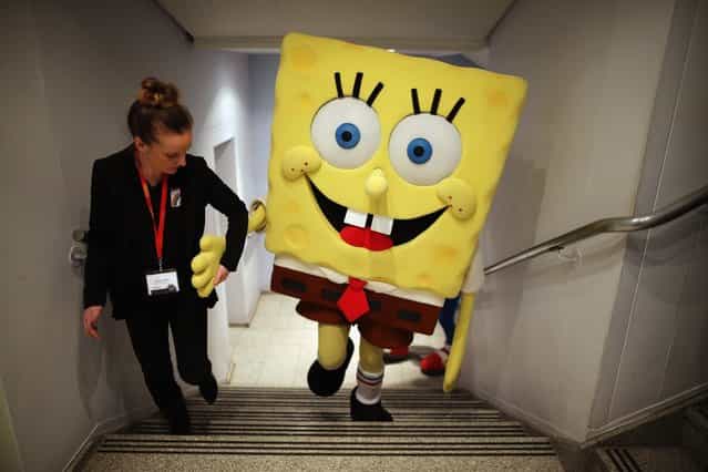 A Sponge Bob Square Pants character is helped up a flight of stairs during the 2013 London Toy Fair at Olympia Exhibition Centre on January 22, 2013 in London, England. The annual fair which is organised by the British Toy and Hobby Association, brings together toy manufacturers and retailers from around the world. (Photo by Dan Kitwood)