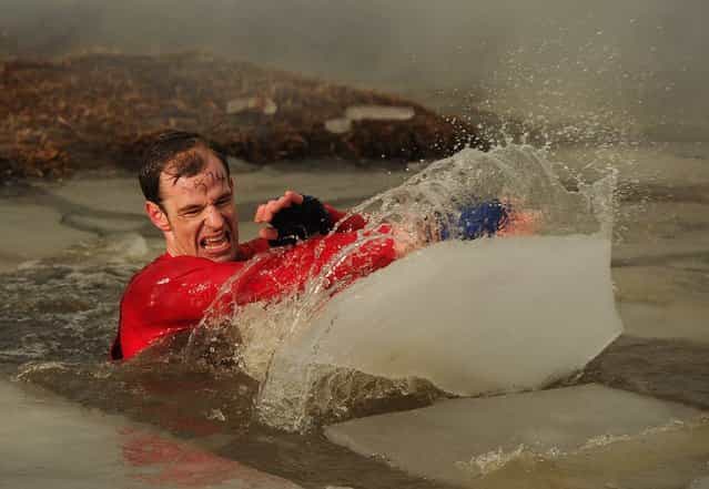 A competitor moves ice from his way as he wades through muddy water during the Tough Guy Challenge endurance race on January 27, 2013 in Telford, England. Every year thousands of people run the 8 mile assault course which involves freezing temperatures, fire and ice. (Photo by Michael Regan)