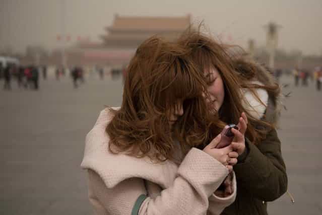 Two women look at a mobile phone as they stand on Tiananmen Square during a sand storm in heavily polluted weather in Beijing on February 28, 2013. Beijing residents were urged to stay indoors as pollution levels soared before a sandstorm brought further misery to China's capital. (Photo by Ed Jones/AFP Photo)