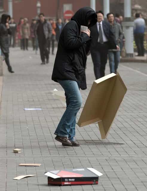 A woman covers her head while walking past a flying cardboard box after the capital city was hit by a sandstorm in Beijing Thursday, February 28, 2013. (Photo by Andy Wong/AP Photo)