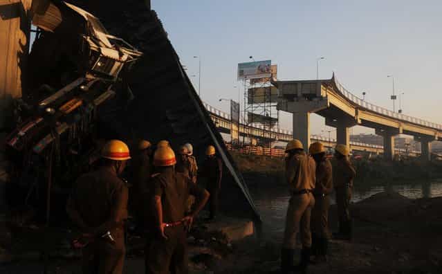 Indian onlookers and firefighters stand near the collapsed portion of a flyover in Kolkata on March 3, 2013. A huge portion of a flyover on the eastern side of the Indian metropolis collapsed leaving three persons injured, the flyover connects the airport with Eastern Metropolitan Bypass and the eastern and southern suburbs. As the debris fell into a canal running below the flyover, it took down a truck the driver and two others were rescued from the canal by fire-brigade personnel and locals. (Photo by Dibyangshu Sarkar/AFP Photo)
