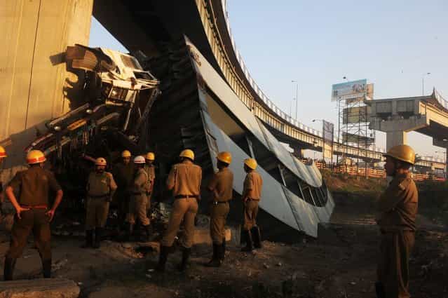 Indian onlookers and firefighters stand near the collapsed portion of the flyover in Kolkata on March 3, 2013. A huge portion of a flyover on the eastern side of the Indian metropolis collapsed leaving three persons injured, the flyover connects the airport with Eastern Metropolitan Bypass and the eastern and southern suburbs. As the debris fell into a canal running below the flyover, it took down a truck the driver and two others were rescued from the canal by fire-brigade personnel and locals. (Photo by Dibyangshu Sarkar/AFP Photo)