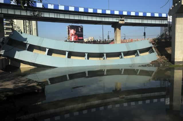 Indian nlookers stand near the collapsed portion of a flyover in Kolkata on March 3, 2013. A huge portion of a flyover on the eastern side of the Indian metropolis collapsed leaving three persons injured, the flyover connects the airport with Eastern Metropolitan Bypass and the eastern and southern suburbs. As the debris fell into a canal running below the flyover, it took down a truck the driver and two others were rescued from the canal by fire-brigade personnel and locals. (Photo by Dibyangshu Sarkar/AFP Photo)