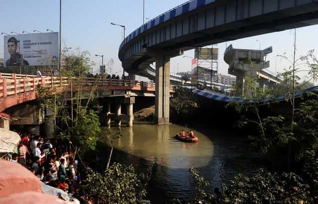 Indian onlookers watch as rescue personnel search waters near the collapsed portion of the flyover in Kolkata on March 3, 2013. A huge portion of a flyover on the eastern side of the Indian metropolis collapsed leaving three persons injured, the flyover connects the airport with Eastern Metropolitan Bypass and the eastern and southern suburbs. As the debris fell into a canal running below the flyover, it took down a truck the driver and two others were rescued from the canal by fire-brigade personnel and locals. (Photo by Dibyangshu Sarkar/AFP Photo)