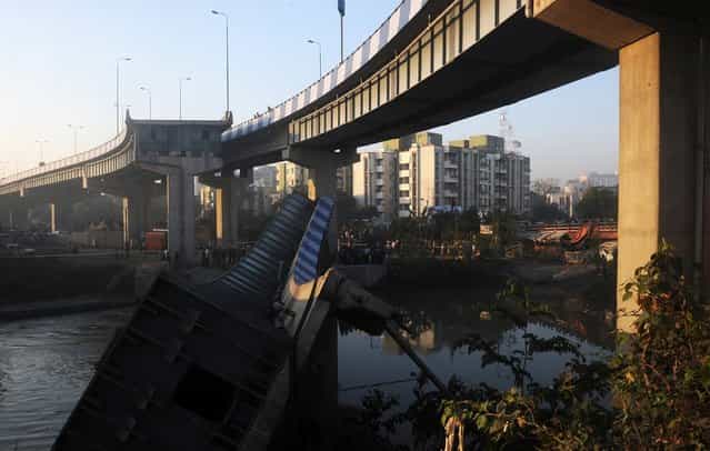 Indian onlookers stand near the collapsed portion of the flyover in Kolkata on March 3, 2013. A huge portion of a flyover on the eastern side of the Indian metropolis collapsed leaving three persons injured, the flyover connects the airport with Eastern Metropolitan Bypass and the eastern and southern suburbs. As the debris fell into a canal running below the flyover, it took down a truck the driver and two others were rescued from the canal by fire-brigade personnel and locals. (Photo by Dibyangshu Sarkar/AFP Photo)