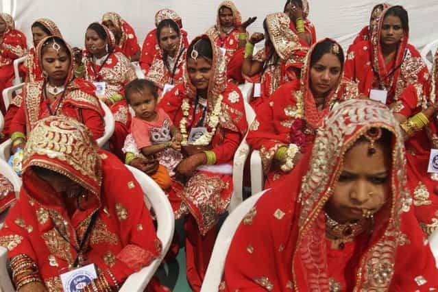 An Indian bride, center, holds a child as she sits with other brides during a mass marriage of 162 Muslim couples in Ahmadabad, India, Sunday, March 3, 2013. Mass marriages in India are organized by social organizations primarily to help the economically backward families who cannot afford the high ceremony costs as well as the customary dowry and expensive gifts that are still prevalent in many communities. (Photo by Ajit Solanki/AP Photo/LaPresse)