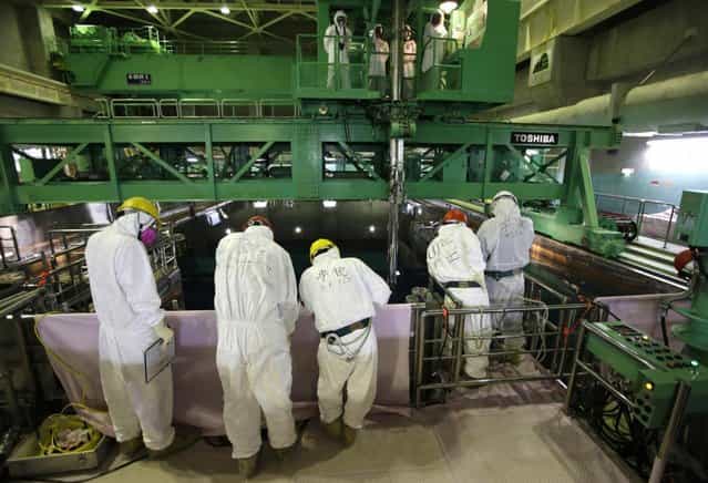 Workers wearing protective suits and masks stand next to the spent fuel pool inside the Common Pool Building, where all the nuclear fuel rods will be stored for decommissioning, at Tokyo Electric Power Co. 's tsunami-crippled Fukushima Dai-ichi nuclear power plant in Okuma, Fukushima prefecture Wednesday, March 6, 2013, ahead of the second anniversary of the March 11, 2011 tsunami and earthquake. Some 110,000 people living around the nuclear plant were evacuated after the massive March 11, 2011, earthquake and tsunami knocked out the plant's power and cooling systems, causing meltdowns in three reactors and spewing radiation into the surrounding air, soil and water. (Photo by Issei Kato/AP Photo/Pool)
