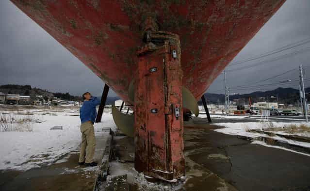 In this Sunday, February 24, 2013 photo, a man inspects a fishing boat which was washed ashore during the March 11, 2011 earthquake and tsunami in Kesennuma, Miyagi Prefecture, Japan. Japan's progress in rebuilding from the tsunami that thundered over coastal sea walls, sweeping entire communities away, is mainly measured in barren foundations and empty spaces. Clearing of forests on higher ground due to be leveled to make space for relocating survivors has barely begun. Japan will next week observes two years from the March 11, 2011 disasters which devastated in the northeastern Pacific coast of the country. (Photo by Junji Kurokawa/AP Photo)