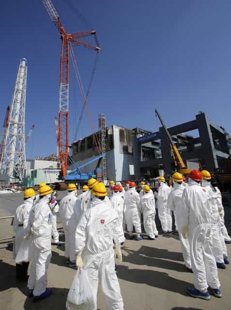 Members of the media wearing protective suits and masks are escorted by TEPCO employees while walking near the building housing the plant's No. 4 reactor, center, and an under construction foundation, right, which will store the reactor's melted fuel rods at Tokyo Electric Power Co.'s Fukushima Dai-ichi nuclear power plant in Fukushima prefecture, Wednesday, March 6, 2013, ahead of the second anniversary of the March 11, 2011 tsunami and earthquake. Some 110,000 people living around the Fukushima Dai-ichi nuclear plant were evacuated after the massive March 11, 2011, earthquake and tsunami knocked out the plant's power and cooling systems, causing meltdowns in three reactors and spewing radiation into the surrounding air, soil and water. (Photo by Issei Kato/AP Photo/Pool)