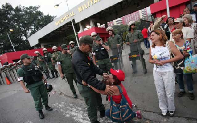 Backed by police, woman kneels in front of the hospital in Caracas, Venezuela, where Hugo Chávez was hospitalized when he died. (Photo by Fernando Llano/AP Photo)