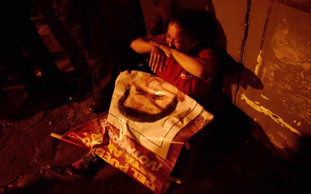 With poster of Hugo Chavez on his lap, woman cries in front of the military hospital where Venezuela's president was hospitalized when he died. (Photo by Leo Ramirez/AFP Photo)