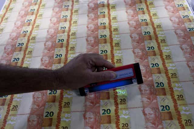 A worker checks the security feature on prints of R$ 20 Brazilian reais bills during the production process at the Casa da Moeda, the national mint, in the Santa Cruz suburb of Rio de Janeiro, Brazil, on Tuesday, March 5, 2013. Brazil is likely to keep its key interest rate at a record low for the third straight meeting, as policy makers are caught between a fragile economic recovery and faster-than-expected inflation. (Photo by Dado Galdieri/Bloomberg)