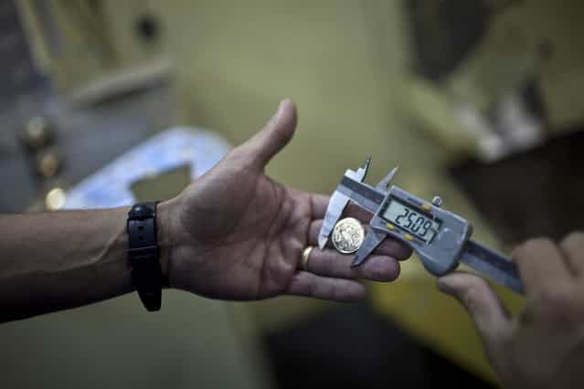 A worker checks the diameter of a R$ 0.25 coin, or 25 centavo, at the Casa da Moeda, the national mint, in the Santa Cruz suburb of Rio de Janeiro, Brazil, on Tuesday, March 5, 2013. Brazil is likely to keep its key interest rate at a record low for the third straight meeting, as policy makers are caught between a fragile economic recovery and faster-than-expected inflation. (Photo by Dado Galdieri/Bloomberg)