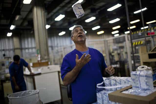 A worker throws a packaged stack R$ 2 Brazilian reais bills totaling R$ 2,000 at the end of the production process at the Casa da Moeda, the national mint, in the Santa Cruz suburb of Rio de Janeiro, Brazil, on Tuesday, March 5, 2013. Brazil is likely to keep its key interest rate at a record low for the third straight meeting, as policy makers are caught between a fragile economic recovery and faster-than-expected inflation. (Photo by Dado Galdieri/Bloomberg)