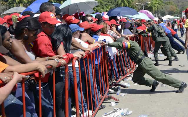 Venezuelan soldiers push the protective fences as supporters wait in line to pay last respects to the late Venezuelan President Hugo Chavez, outside the Military Academy in Caracas on March 7, 2013. Venezuelans filed past the open casket of late President Hugo Chavez as he lay in state after throngs of weeping loyalists gave the firebrand leftist a rousing farewell on the streets on the eve. (Photo by Leo Ramirez/AFP Photo)