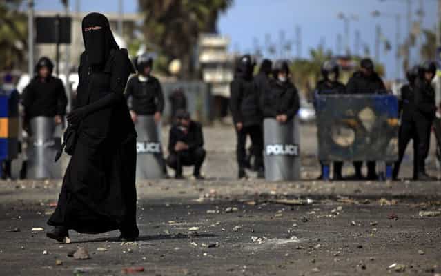 A woman walks past riot police, background, during clashes with protesters, unseen, near a state security building in Port Said, Egypt, Thursday, March 7, 2013. Clashes between protesters and police continued into a fifth day on Thursday in the restive Egyptian city of Port Said. (Photo by Khalil Hamra/AP Photo)