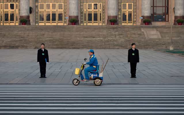 A street cleaner on an electronic bike passes by People's Liberation Army soldiers dressed as ushers while they stand guard in front of the Great Hall of the People before the opening session of the National People's Congress in Beijing Tuesday, March 5, 2013. In a rare move, China declined to reveal its defense budget request for 2013. Every year, the country announces its defense spending plan for the upcoming year at a press conference before the opening of an annual session of the National People's Congress, China's parliament. (Photo by Andy Wong/AP Photo)