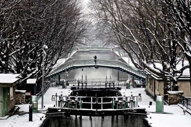 A person takes a photo from a bridge, at the canal St Martin, in Paris, on March 12, 2013. Hundreds of flights out of Western Europe have been cancelled, no trains running under the English Channel, and Belgium's prince is stuck at home, all because of a sudden dump of oddly late snowfall on Western Europe. (Photo by Thibault Camus/Associated Press)