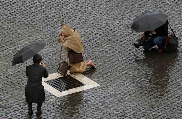 A man dressed as a monk kneels as he waits for the start of the conclave in Saint Peter's Square at the Vatican March 12, 2013. The doors of the Sistine Chapel shut on Tuesday, leaving 115 Roman Catholic cardinals inside to start a conclave to elect the next pope. (Photo by Max Rossi/Reuters)