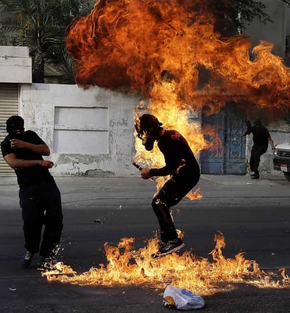 An anti-government protester is engulfed in flames after a shot fired by police hit the petrol bomb he was preparing to throw during clashes in Sanabis, Bahrain, on March 14, 2013. Protests and clashes erupted nationwide as government opponents called a [Dignity Strike], blocking roads, closing shops, protesting and staying home from work and school. (Photo by Hasan Jamali/Associated Press)