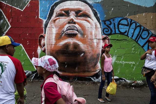 People walk by graffiti showing the late Venezuelan President Hugo Chavez, as they head to pay their final respects during Chavez's funeral ceremony at the military academy in Caracas, on March 11, 2013. (Photo by Mauricio Lima/The New York Times)