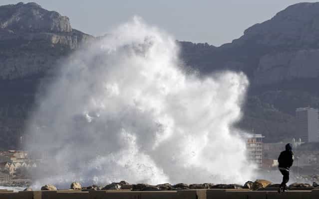 A passer-by walks as a high wave hits the waterfront in Marseille March 14, 2013. French public weather agency Meteo France issued an orange alert warning of winds threatening southern French departments. (Photo by Jean-Paul Pelissier/Reuters)