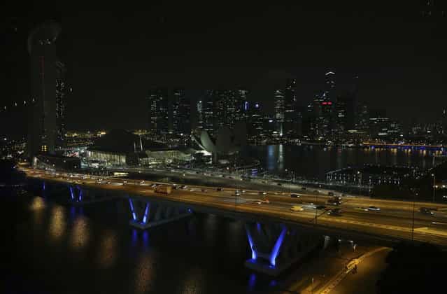 The Singapore city-skyline is seen in darkness against the lit highway as lights in major buildings around the financial district are switched off for a whole hour on Saturday, March 23, 2013 in Singapore. More than 100 buildings, locations and organizations in Singapore switched off their lights as part of the global Earth Hour initiative by World Wide Fund for Nature (WWF) along with other national monuments around the world. (Photo by Wong Maye-E/AP Photo)