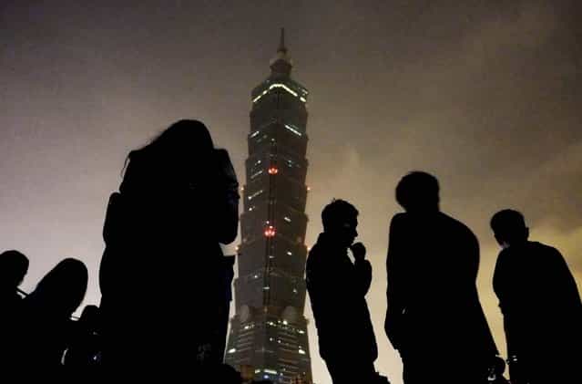 Onlookers watch Taipei 101 building as it turns its lights off to observe international [Earth Hour] in Taiwan, on March 23, 2013. Around 100 people gathered outside the skyscraper Saturday, using energy saving LED lights to observe the global event that encourages people to turn off their lights for an hour. (Photo by Wally Santana/Associated Press)