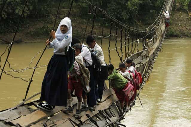 Students hold on to the side steel bars of a collapsed bridge as they cross a river to get to school at Sanghiang Tanjung village in Lebak regency, Indonesia's Banten village January 19, 2012. Flooding from the Ciberang river broke a pillar supporting the suspension bridge, which was built in 2001, on Monday according to Epi Sopian the head of Sanghiang Tanjung village. Sofiah, a student crossing the bridge, says she will need to walk for an extra 30 minutes if she were to take a detour through another bridge. (Photo by Beawiharta/Reuters)