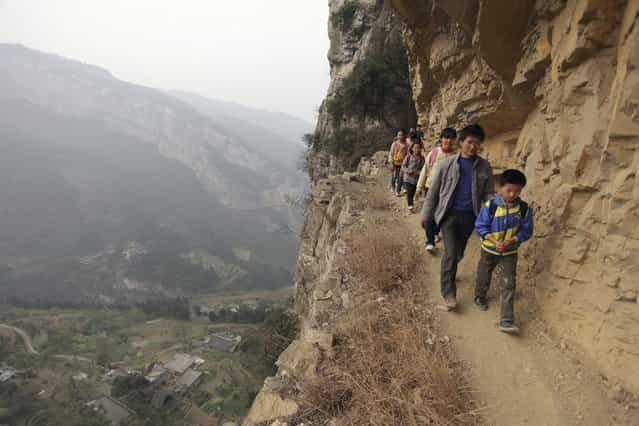 Xu Liangfan, 37, escorts students on a cliff path as they make their way to Banpo Primary School in Guizhou province March 12, 2013. Located halfway up a mountain, the school has 68 students of which about 20 live in the nearby Gengguan village. Students from Gengguan have to edge their way along the narrow cliff path to go to class everyday, alongside Xu who would escort them. The path, which was carved from cliffs over 40 years ago, is the only route between Gengguan village and the school, according to local media. Picture taken March 12, 2013. (Photo by Reuters/Stringer)