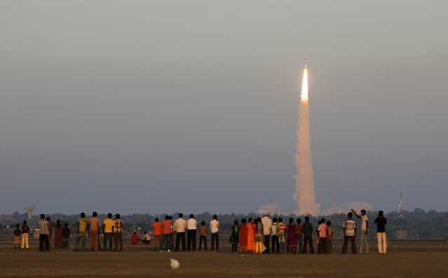 Onlookers watch as the Indian Space Research Organization’s Polar Satellite Launch Vehicle (PSLV-C20) lifts off from the Satish Dhawan Space Center in Sriharikota, India, on February 25, 2013. The rocket successfully launched the SARAL oceanographic satellite and six other spacecraft. (Photo by Arun Sankar K./AP Photo)