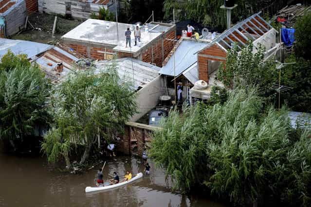 Residents stand on the roof of their homes while others paddle through a flooded street after heavy rains flooded a large part of the city, in La Plata April 3, 2013. At least 46 people were killed in Argentina on Wednesday after a torrential downpour battered the eastern city of La Plata and forced some 2,200 people to flee their homes in search of dry ground. (Photo by Reuters/Infobae.com)