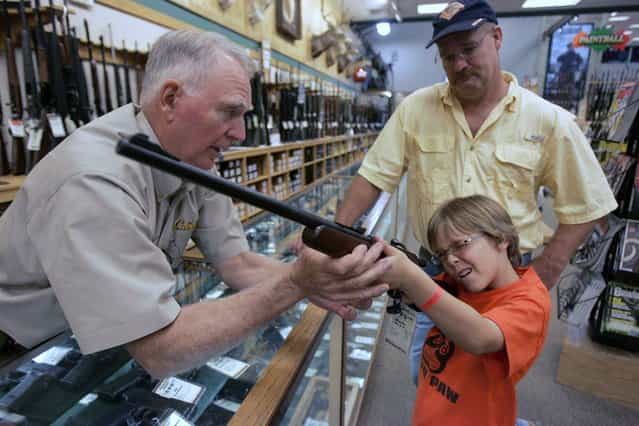 Hunter McConathy (C), 7, holds a hunting rifle with a short stock as his father Bryan (R) and Cabela's salesman Russ Duncan (L) watch him at the Cabela's store in Fort Worth, Texas June 26, 2008. Individual Americans have a right to own guns, the Supreme Court ruled on Thursday for the first time in history, striking down a strict gun control law in the U.S. capital. (Photo by Jessica Rinaldi/Reuters)