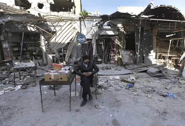 A Syrian street vendor who sells cigarette boxes, sits in front of destroyed shops which were damaged by the shelling of the Syrian forces, at Maarat al-Nuaman town, in Idlib province, on February 26, 2013. Syrian rebels battled government troops near a landmark 12th century mosque in the northern city of Aleppo on Tuesday, while fierce clashes raged around a police academy west of the city, activists said. (Photo by Hussein Malla/AP Photo /The Atlantic)