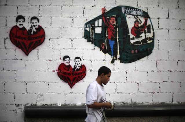 A street artist stands in front of a wall with graffiti showing late Venezuela President Hugo Chavez and current acting President and presidential candidate Nicolas Maduro in Caracas April 10, 2013. Venezuelans will hold presidential elections on April 14. The graffiti (L and C) read, [We are all Chavez]. (Photo by Tomas Bravo/Reuters)