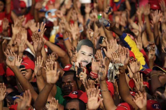 Supporters wave their hands as one of them holds a mask of Venezuela's acting President Nicolas Maduro during a campaign rally in Catia La Mar, Venezuela, Tuesday, April 9, 2013. Maduro, the hand-picked successor of late President Hugo Chavez, is running for president against opposition candidate Henrique Capriles in the presidential election set for Sunday, April 14. (Photo by Ariana Cubillos/AP Photo)